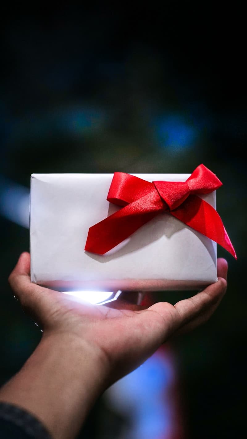 Manos sosteniendo y entregando una caja de regalo envuelta con lazo